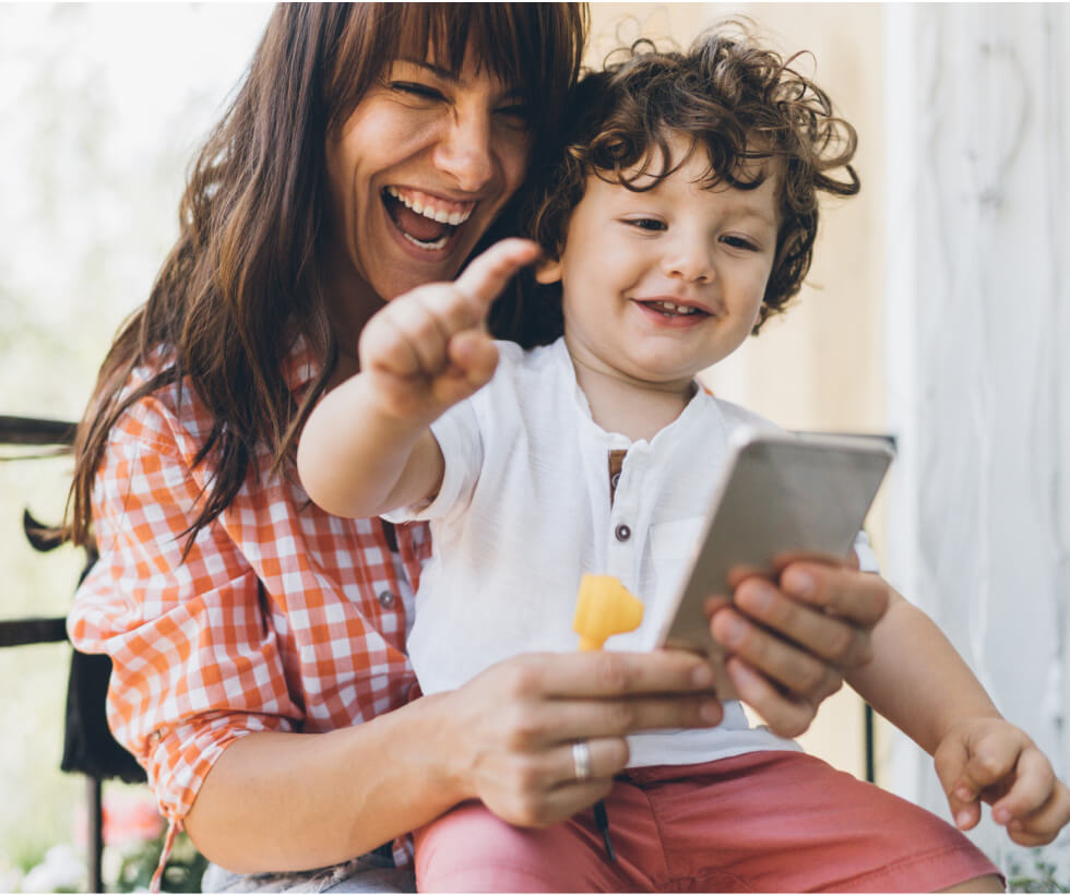 Mom holding a toddler, both looking at a smartphone